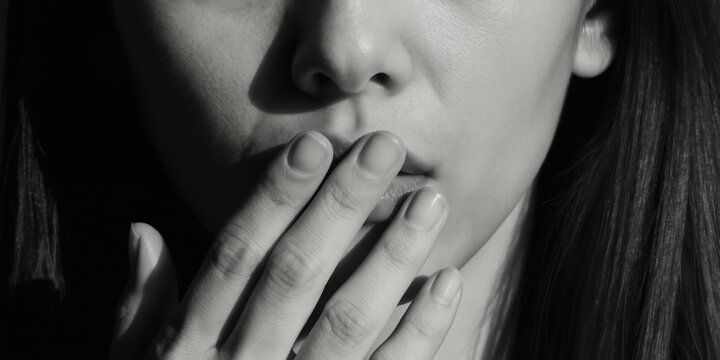 Monochrome portrait shows woman covering mouth with hand. Face shows deep emotion. Dark shadows add mystery and drama. Gesture implies secrecy or fear.