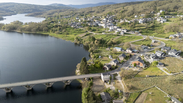 Aerial view of Encoro de Prada reservoir and the village of A Veiga with a stone bridge and green hills in A Veiga, Ourense, Spain.