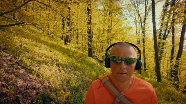 A modern mature man in his 50s using wireless headphones and sunglasses while hiking. Intersection of technology, gadgets, and active outdoor lifestyle. 4k quality.