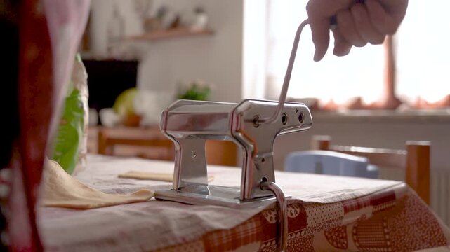 hand of old italian grandma making fresh handmade tagliatelle pasta with manual pasta machine, italian food with warm natural light, healthy nutrition