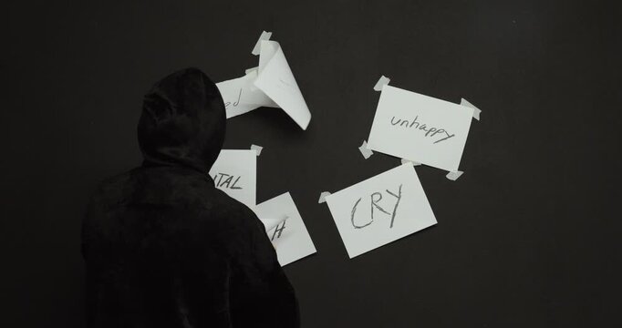 Man taking down words like sad and unhappy from a wall, symbolizing recovery, healing, and overcoming negative emotions.