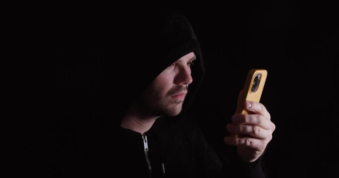 Man in a dark hoodie using a smartphone, representing social media use, digital behavior, and online interaction.