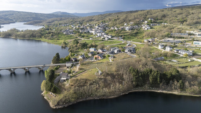 Aerial view of Encoro de Prada reservoir and the village of A Veiga with its stone bridge and surrounding green hills in A Veiga, Ourense, Spain.