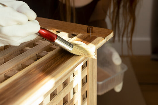 Gloved hand applies finish to a wooden storage table. Warm light highlights the lattice surface and natural grain. DIY furniture restoration for home improvement..