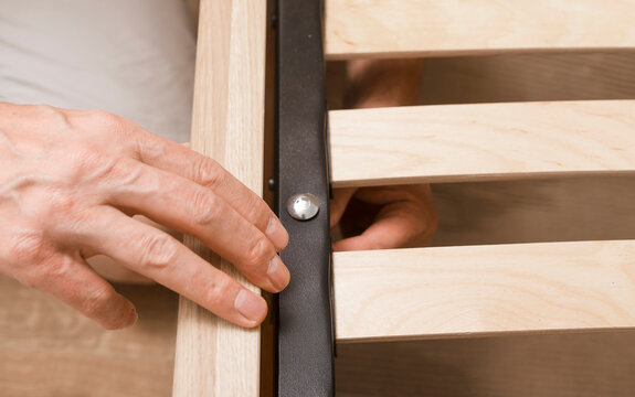 Hand adjusting a wooden bed frame during assembly. Close up of furniture hardware and slatted timber parts in a home setup. DIY installation and interior improvement concept..