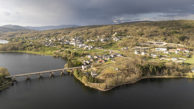 Aerial view of Encoro de Prada reservoir and the village of A Veiga with its stone bridge and surrounding green hills in A Veiga, Ourense, Spain.