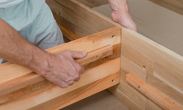 Wooden furniture assembly with hands fitting a timber joint. Close up of carpentry work in an indoor workshop. Home improvement and woodworking installation concept..