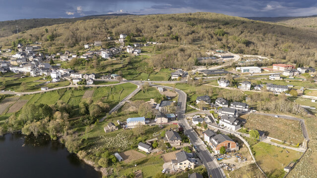 Aerial view of Encoro de Prada reservoir and the village of A Veiga with stone houses, green meadows, and forested hills in A Veiga, Ourense, Spain.
