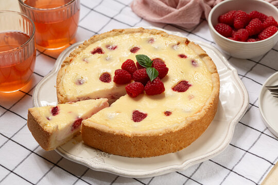 Homemade baked cheesecake with fresh raspberries. Kompot drink. Beige table with textile runner.