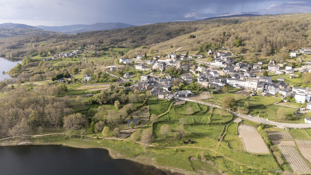 Aerial view of the village of A Veiga and the Encoro de Prada reservoir surrounded by lush green hills and stone houses in A Veiga, Ourense, Spain.