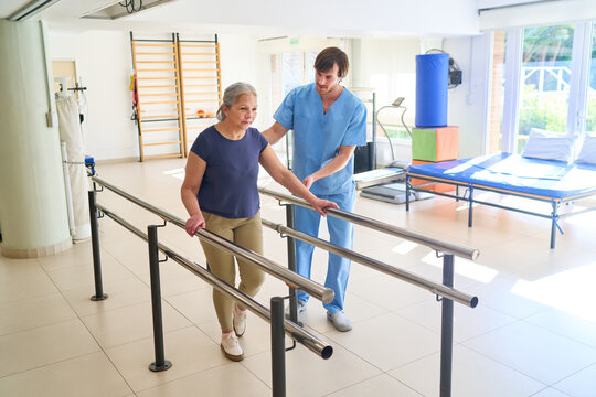 Senior Woman Walking with Physiotherapist in Rehab Center Using Parallel Bars for Rehabilitation and Physical Therapy Indoors