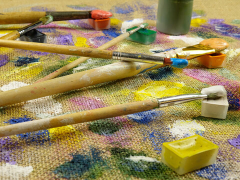 Various multi-colored spots of different shapes from paint brushes with gouache and acrylic paint on the beige burlap fabric, abstract background