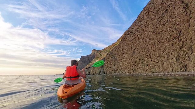 Kayak ocean sunset man paddling an orange boat near rocky cliffs during a peaceful evening adventure in the sea