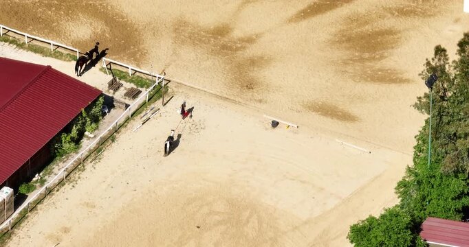 Aerial view of a sand-covered equestrian arena where a person is leading a horse in a circular training exercise, showcasing the textured ground and the focused bond of horse and trainer.