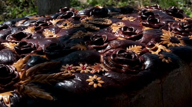 A large traditional korovai bread baked for a 70th anniversary is displayed outdoors in bright sunlight. The number 70 is formed in the center, surrounded by decorative dough .