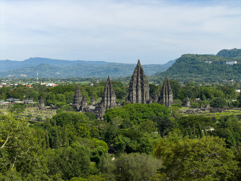 Aerial view of Prambanan Temple, the ancient Hindu temple complex surrounded by lush tropical trees and distant mountains under a clear sky Prambanan, Daerah Istimewa Yogya, Indonesia.