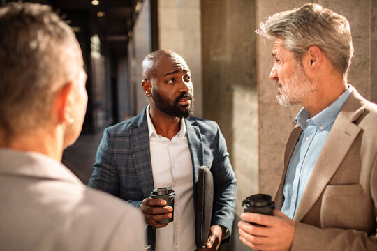 Three business colleagues discussing work over coffee outside an office building