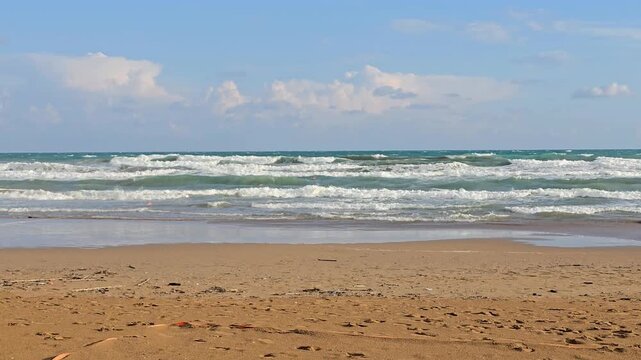 Powerful ocean waves rolling onto a golden sandy beach under a blue sky