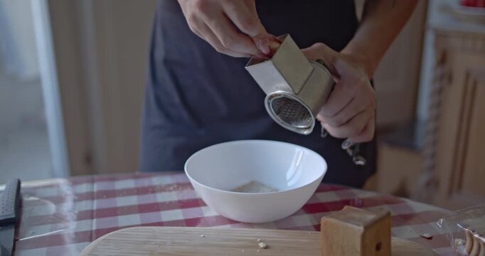 A shot shows a person's hands using a manual grater to create fresh breadcrumbs into a white bowl. This is perfect for culinary content, cooking tutorials, or showcasing homemade food preparation.