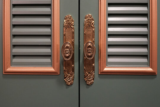 Ornate vintage door handles on green cabinet doors with symmetrical design, decorative metal hardware detail, classic interior architecture texture, luxury furniture close up background concept