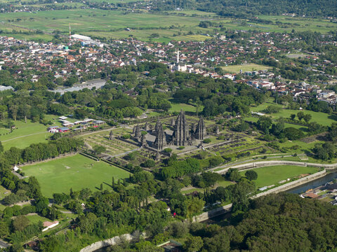 Aerial view of Prambanan Temple complex with its towering stone spires surrounded by lush green lawns and the nearby urban landscape Prambanan, Daerah Istimewa Yogya, Indonesia.