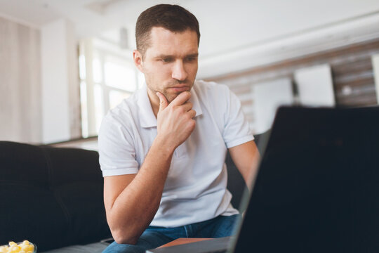 Young man watch tv in his own apartment. Concentrated confident guy watching sport match, game or program. Also watch movie or film. Intension looking at screen.