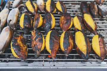 Close up of grilled Silver Bluggoe bananas on charcoal. Thai street food snack featuring roasted plantain with golden flesh and charred skin. Authentic Asian culinary lifestyle background. © The Dell Shot by SJ