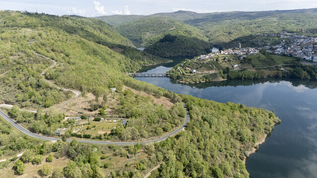 Aerial view of the Bibei River winding through lush green hills and a historic town with a bridge crossing the water Viana do Bolo, Province of Ourense, Spain.