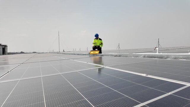 Worker in high-visibility gear installs solar panels on a rooftop under a cloudy sky