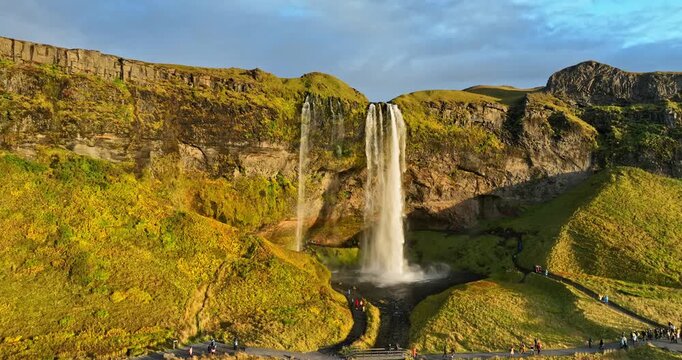 Aerial view of Seljalandsfoss in Iceland with sweeping trail network, visitor access, and dramatic waterfall scenery across glowing volcanic terrain.