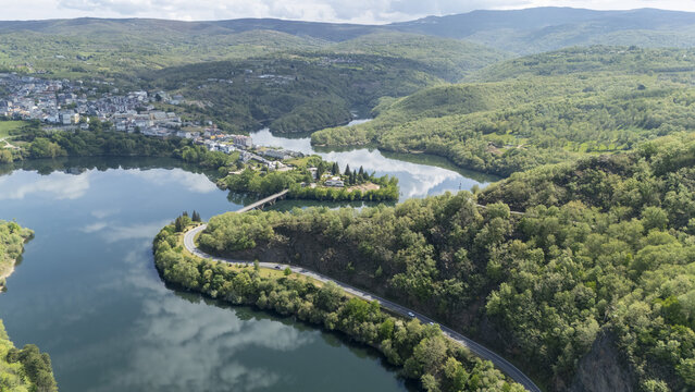 Aerial view of the town of Viana do Bolo situated along the calm reservoir waters, surrounded by lush green forests and rolling hills in Viana do Bolo, Province of Ourense, Spain.