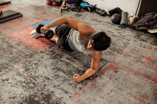 Young Asian man does side plank with lateral raise at the gym improving core strength and shoulder stability through controlled resistance exercise