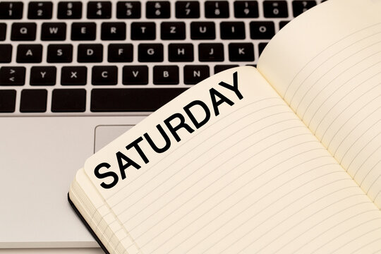 Notebook with Saturday written on blank page next to laptop keyboard in a workspace setup
