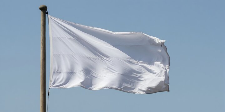 White cloth flag waves on wooden pole against clear blue sky. Fabric flutters in the wind, signifying peace, surrender, or neutrality in breezy weather conditions. Symbol of peace.