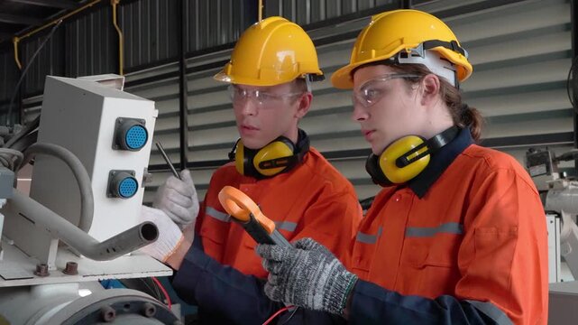 Industrial workers in hard hats and safety gear inspect machinery with tools