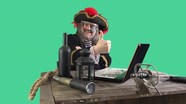 A pirate-costumed man at a desk with a laptop, spyglass and gold coins, isolated on green screen &mdash; a funny parody of internet piracy, illegal downloading and copyright infringement
