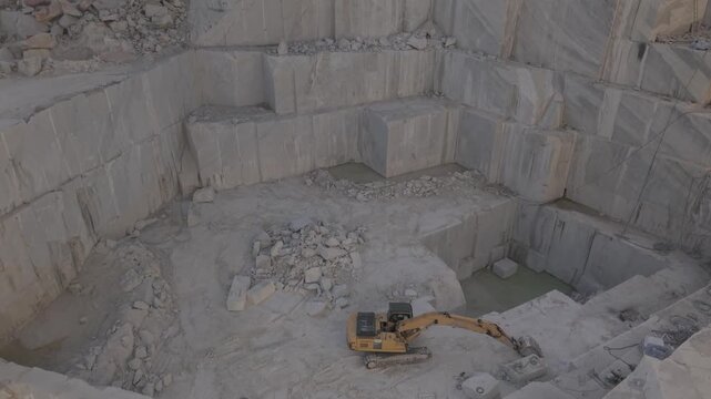Wide angle view of a deep marble quarry with heavy machinery, excavators, and stone blocks in a stepped open-pit mine.