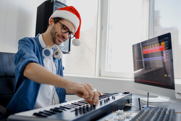 Merry Christmas and a happy new year! Composer hands on piano keys in recording studio. music production technology, man in christmas hat is working on pianino and computer keyboard on desk. © Vlad
