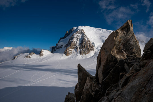 Mont blanc du Tacul (4,284 m) peak rises under a clear blue sky, overlooking the vast snow-covered Vall&eacute;e Blanche glacier with dark rock formations in the foreground, Chamonix, France - stock photo