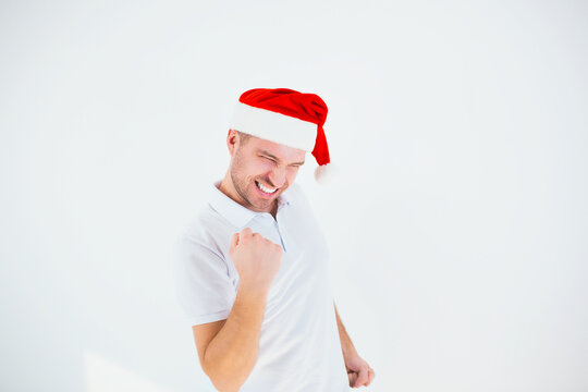 Young man isolated over white background. Guy cheering and in joyful mood. Alone in studio wearing santa hat. Christmas time or new year period. Positive energetic man.