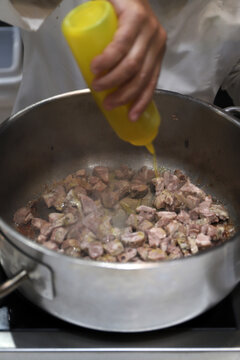 chef cocinando carne en una olla y echando aceite al guiso