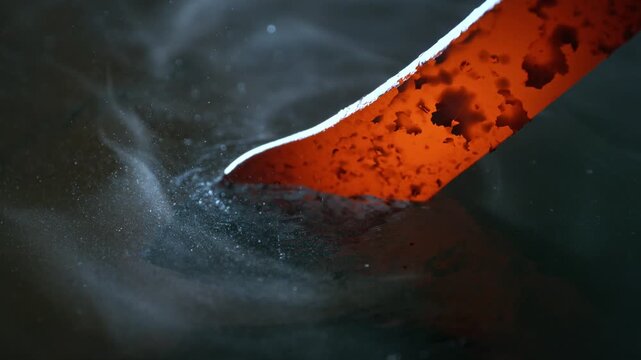Blacksmith puts the red-hot forged metal part into the water . Super slow motion filmed on high speed cinematic camera at 1000 fps