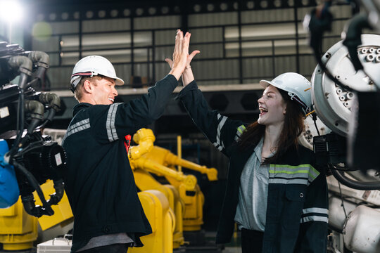 Industrial engineer teamwork factory machinery safety helmet uniform robotics collaboration Two industrial engineers wearing safety helmets and uniforms celebrate teamwork with high five modern