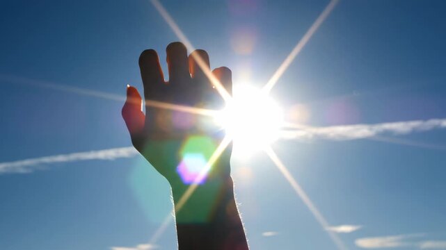 Silhouette of hand reaching for sun in blue sky