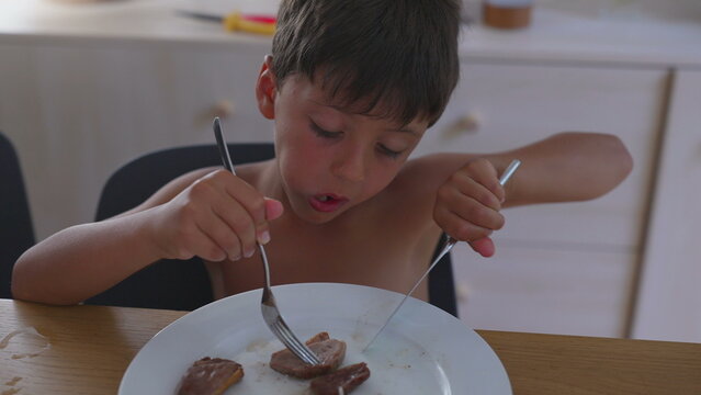 Boy eating steak at the table using fork and knife, showing focus and independence while practicing self-feeding skills during mealtime indoors