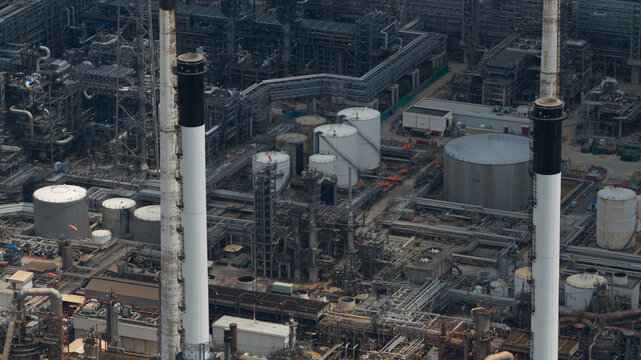 Aerial view of Bangchak Sriracha Refinery featuring tall industrial chimneys, storage tanks, and complex piping systems in Si Racha District, Chon Buri, Thailand.