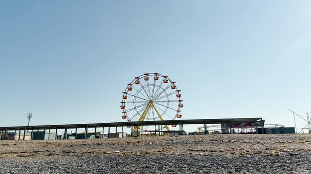 The distant amusement wheel stands over the empty coastline. Continuous ocean waves roll onto the pebble beach, making a rhythmic, soothing sound of the rushing surf.