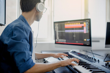 composer hands on piano keys in recording studio. music production technology, man is working on pianino and computer keyboard on desk. © Vlad