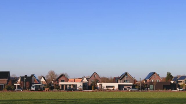 Row of luxury Dutch houses in front of a sunny grass meadow and passing cars in Doesburg, The Netherlands