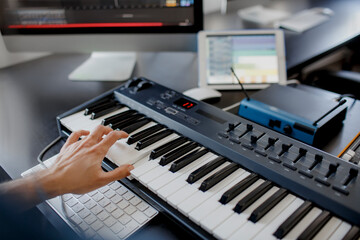 composer hands on piano keys in recording studio. music production technology, man is working on pianino and computer keyboard on desk. close up concept. © Vlad